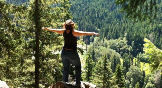 A photo of Angie Ebba, a woman with ankylosing spondylitis, fibromyalgia and migraine standing on top of a mountain after a hike.